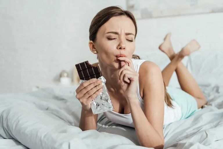 Femme mangeant du chocolat noir le soir dans son lit, illustrant l’impact possible sur l’endormissement.
